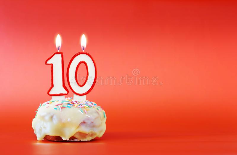 tien-jaar-verjaardags-cupcake-met-witte-brandende-kaars-de-vorm-van-nummer-levendige-rode-achtergrond-exemplaarruimte-142905614